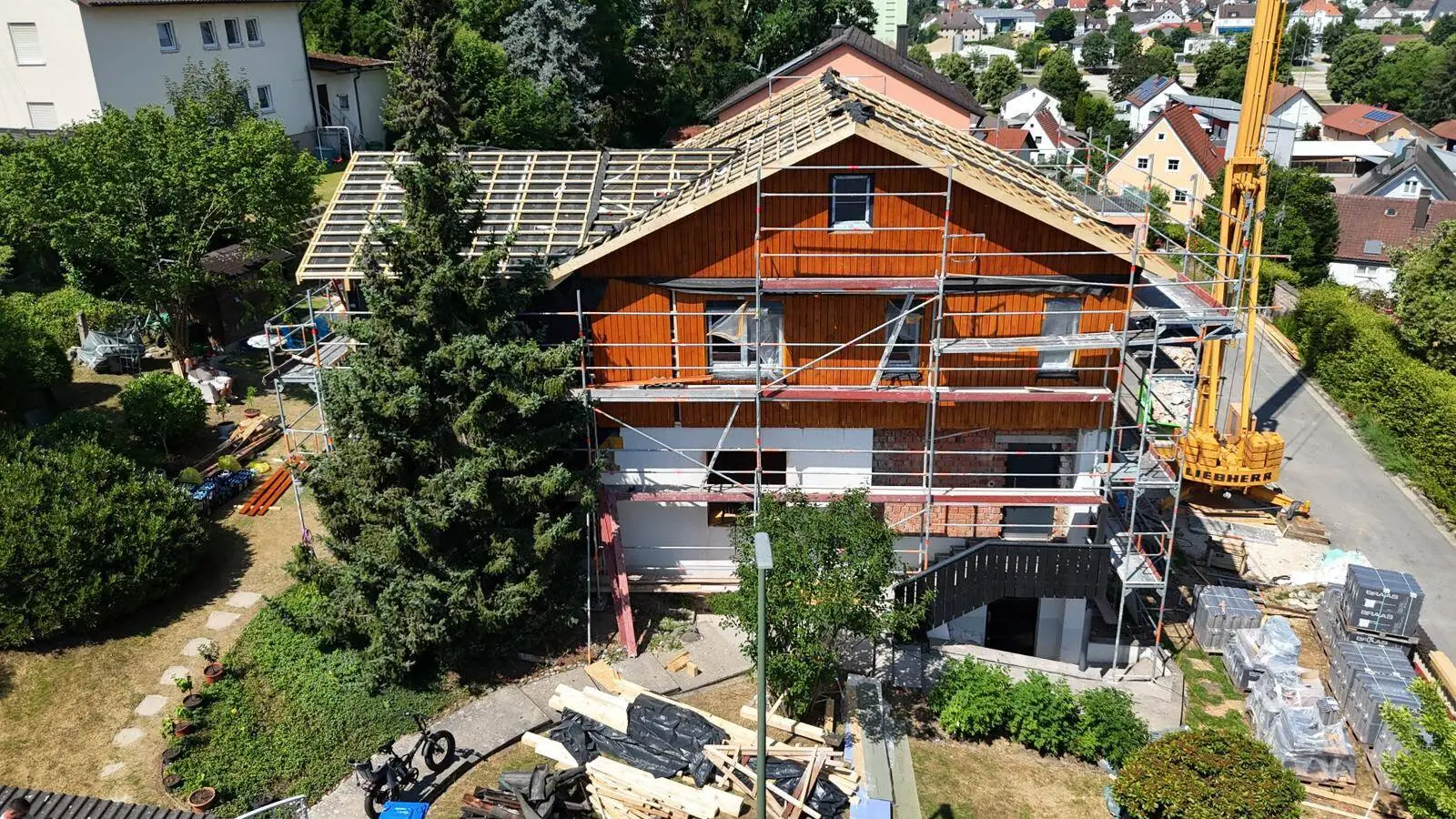 Einfamilienhaus im Bau: Giebelseite mit neuer Holzfassade, offener Dachstuhl und Baugerüst, Kran an der Straßenseite