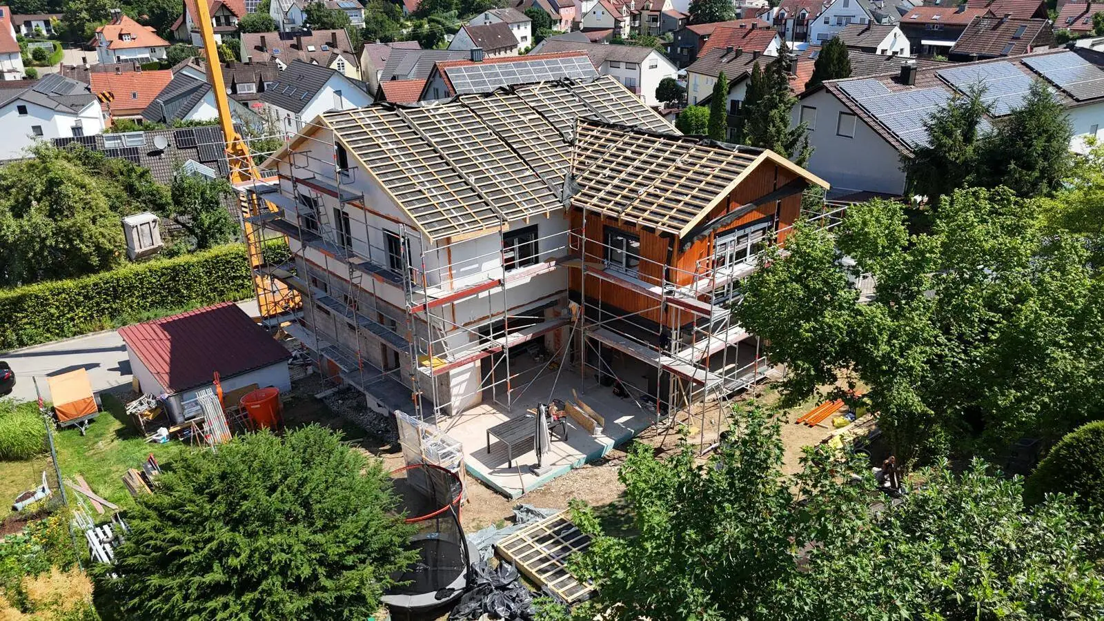 Luftaufnahme der Baustelle: neue Dachkonstruktion mit Lattung, Holzfassade am Anbau, Gerüst rundum