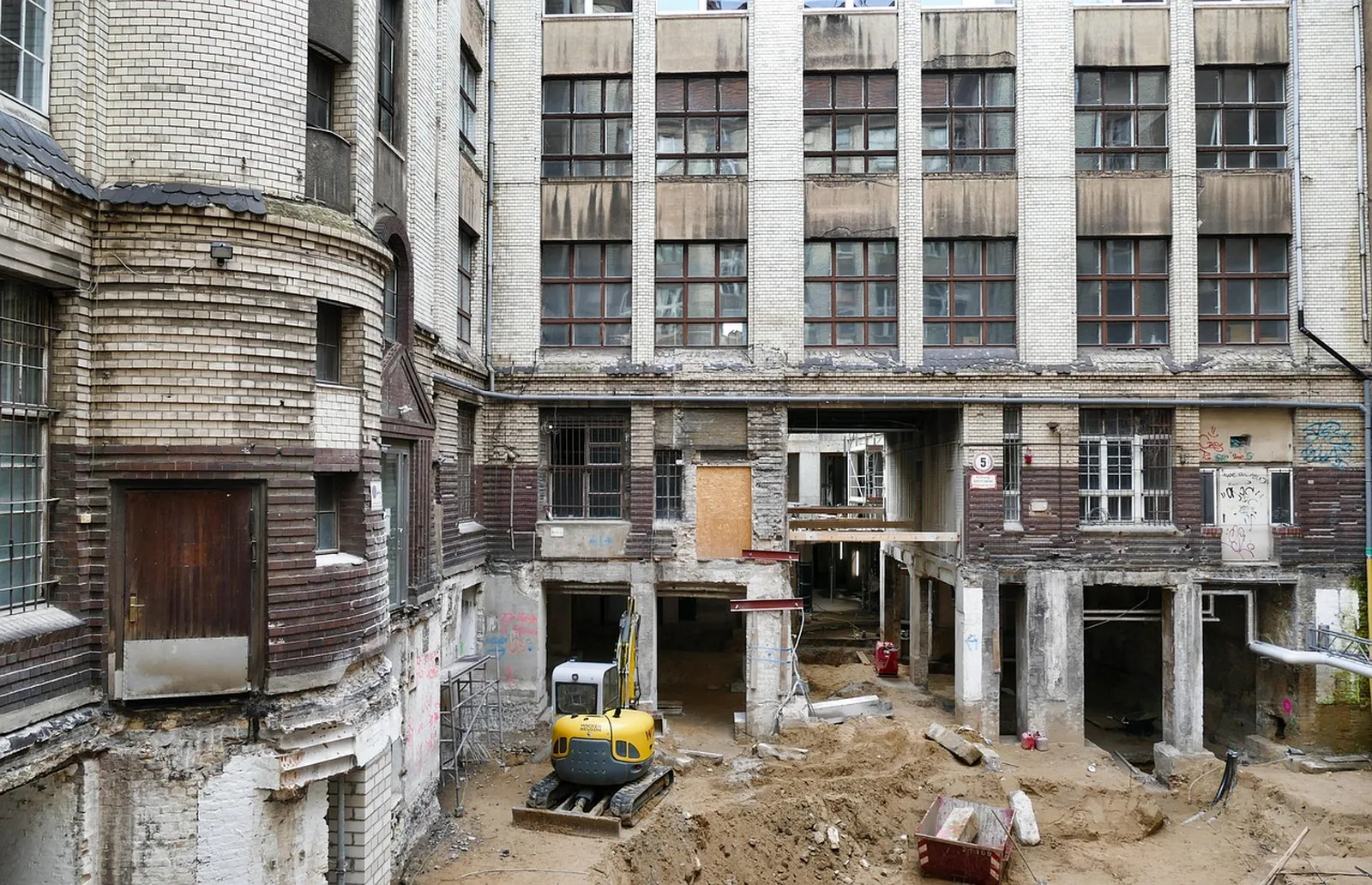 Entkerntes Bestandsgebäude mit freigelegtem Mauerwerk und Baumaschine davor