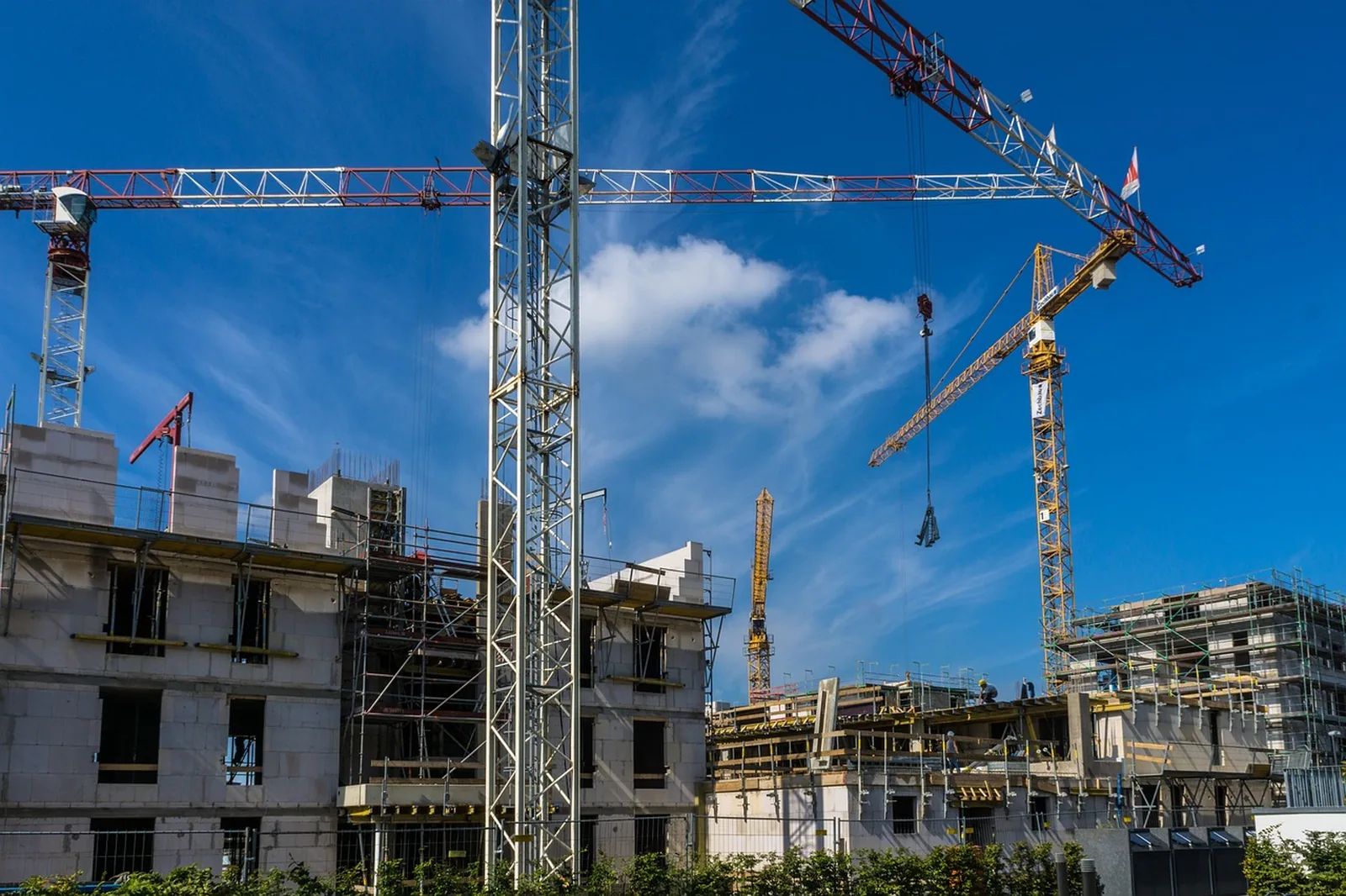 Zwei Turmdrehkrane über einem mehrgeschossigen Neubau vor blauem Himmel