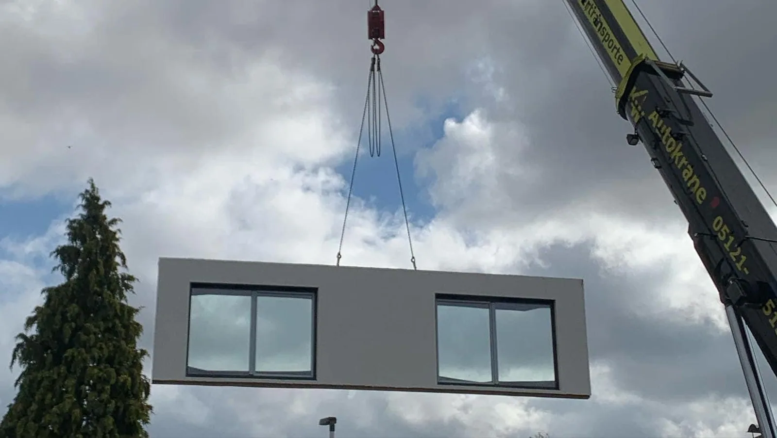 Ein Autokran setzt ein vorgefertigtes Wandelement über der Baustelle ab